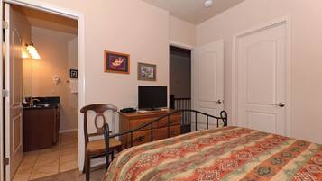 A bedroom with a bed, a desk with a computer, a chair, a dresser, and a door.