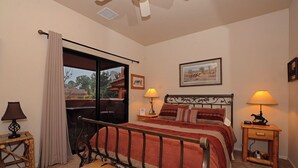 Ein Schlafzimmer mit einem Bett, zwei Nachttischen mit Lampen, einem Fenster mit Vorhängen und einem Deckenventilator.