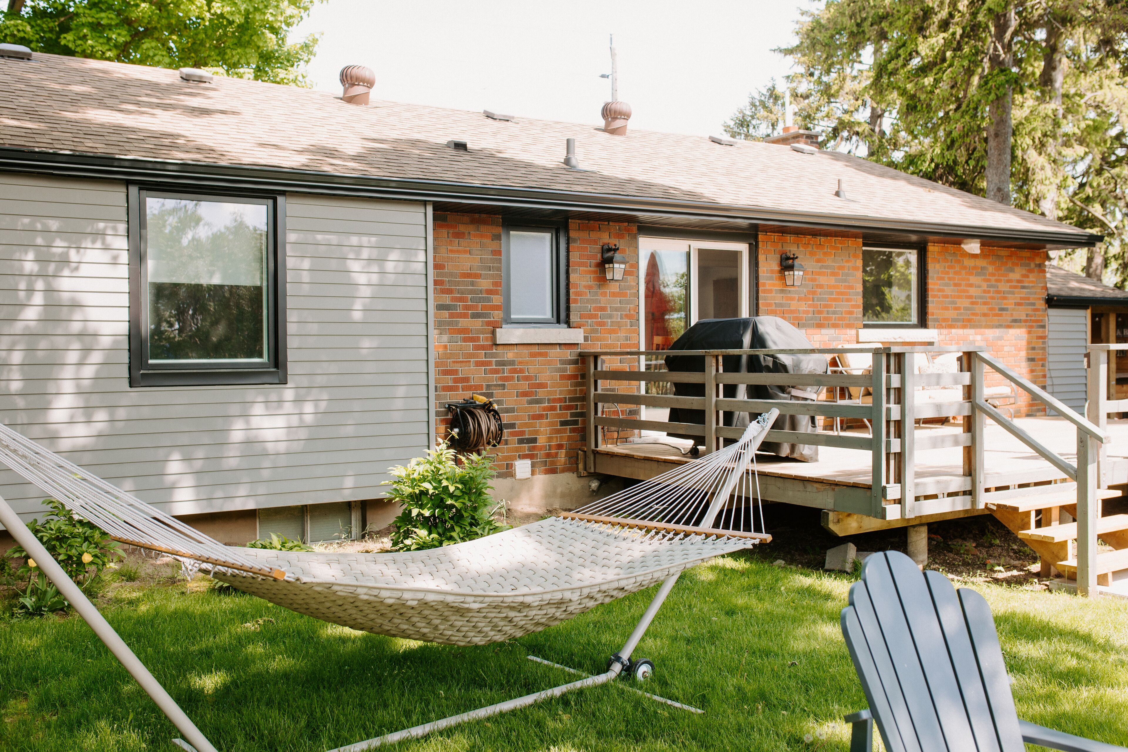 Une maison avec une façade en briques, une terrasse en bois, un hamac et un espace barbecue.