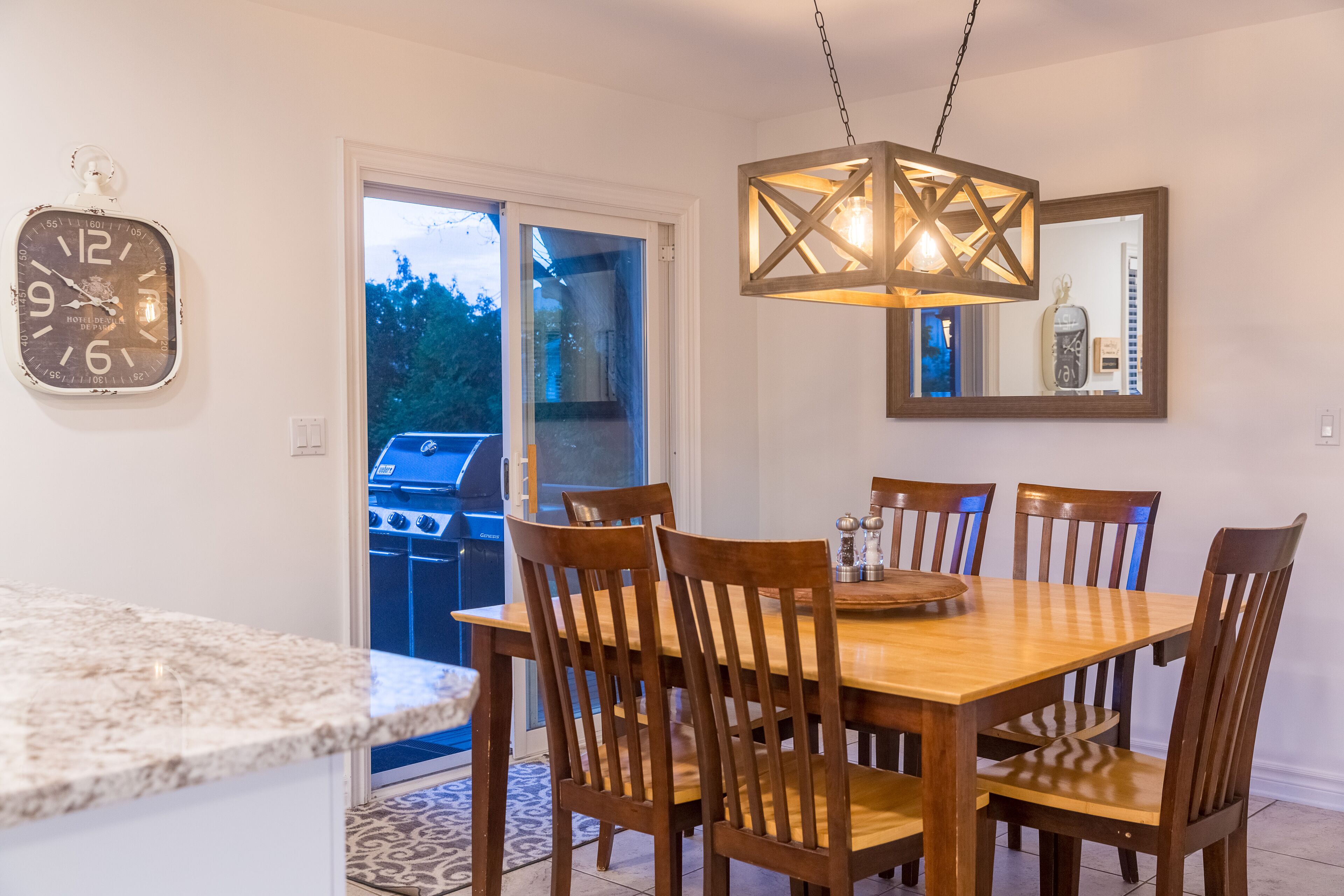 Un comedor con una mesa y sillas de madera, una lámpara colgante y un reloj en la pared.