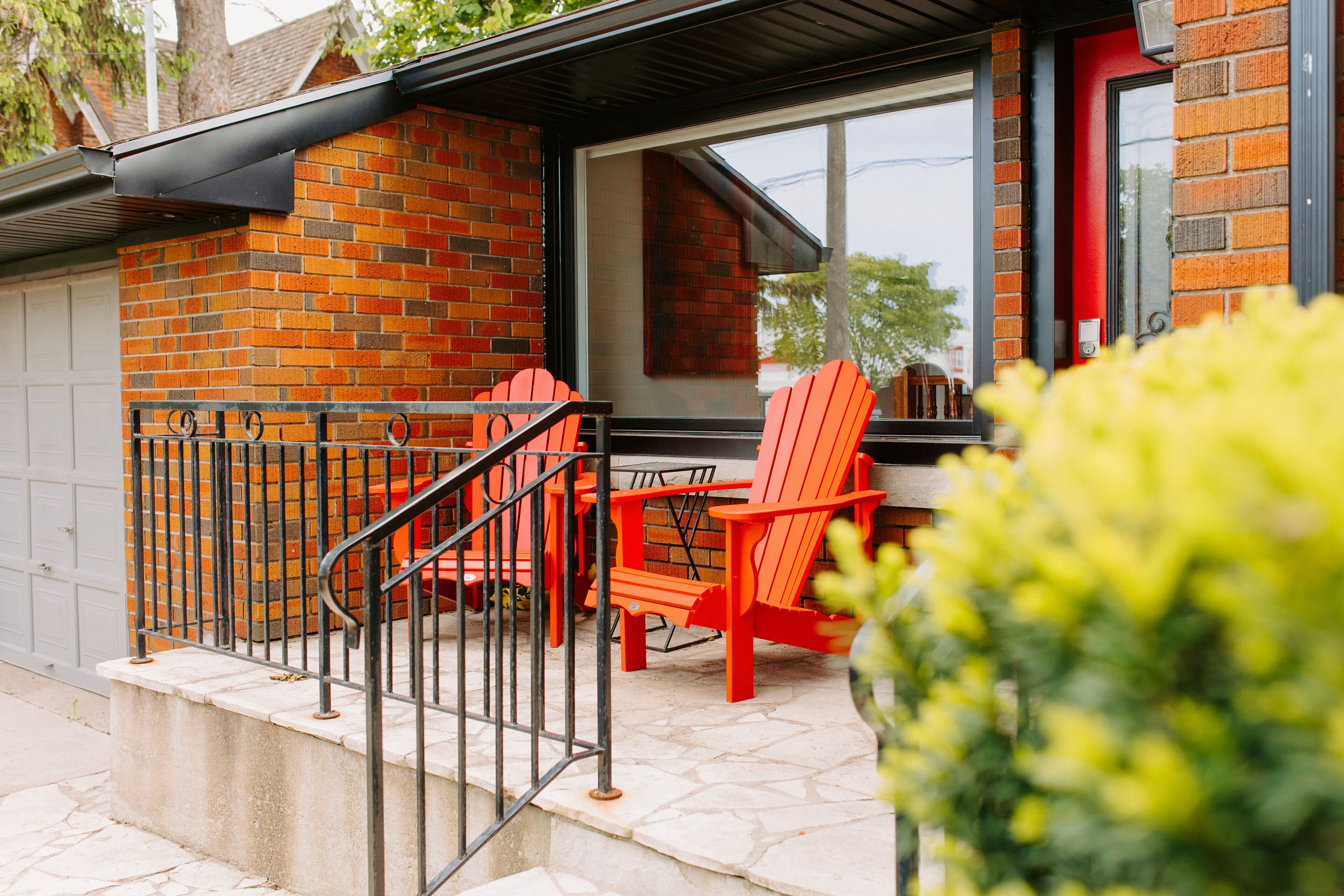 A brick exterior with a glass door, outdoor seating with red chairs, and a metal railing.