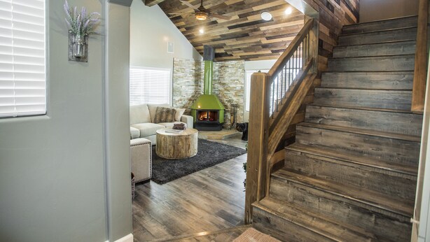 Una escalera de madera con peldaños y barandilla, que conduce a una sala de estar con chimenea, sofá y mesa de centro.