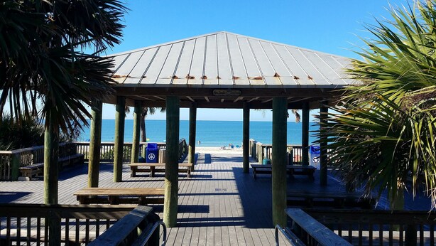 A wooden gazebo with a metal roof, surrounded by wooden benches and palm trees, overlooking a beach. - 30 Seconds to Beach Path! All inclusive! Kayaks, SUP's, Bikes & so much more!!! (Englwood)