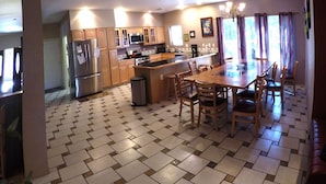 Una cucina con pavimento piastrellato, mobili in legno, frigorifero, microonde, piano cottura e tavolo da pranzo con sedie.