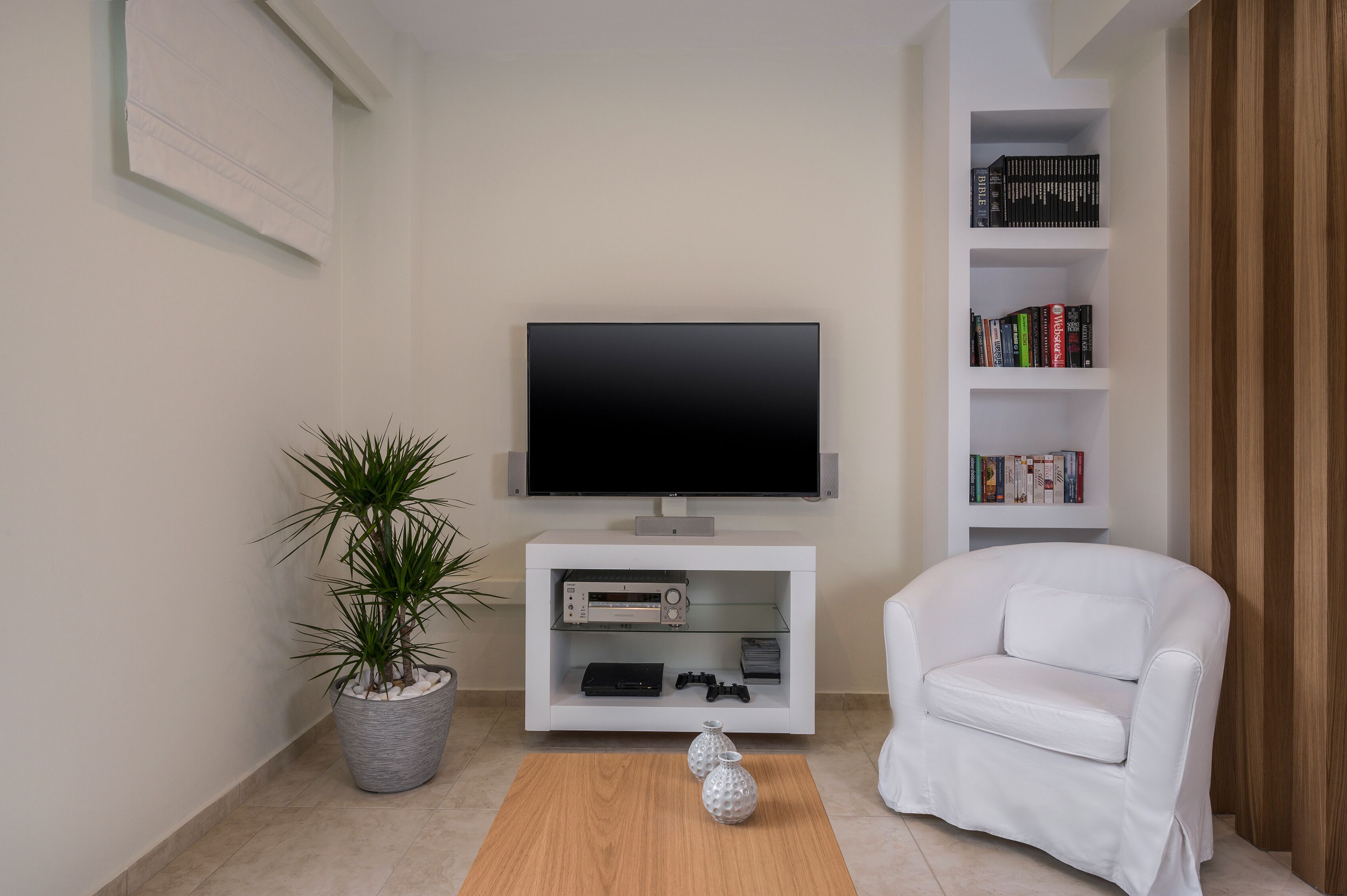 Una sala de estar moderna con un televisor de pantalla plana, un sofá blanco, una estantería y una planta en maceta.
