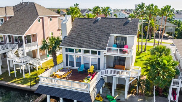 A waterfront house with a deck, outdoor seating, and kayaks.