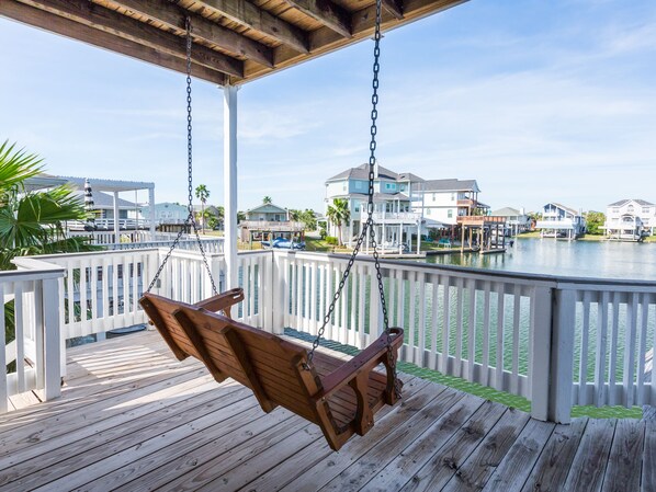 Una silla mecedora de madera en una terraza de madera con vistas a un puerto deportivo con casas y barcos.
