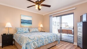 A bedroom with a bed, two bedside tables, a ceiling fan, a painting, and a view through a sliding glass door.
