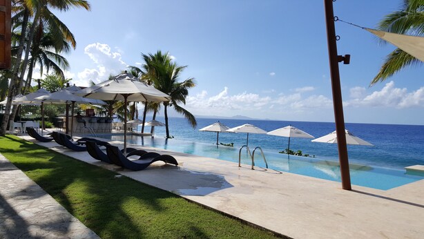 Uma área à beira da piscina com espreguiçadeiras e guarda-sóis, um bar e vista para o oceano.