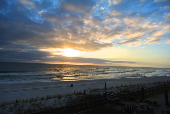 A beach with a wooden walkway and benches, overlooking the ocean at sunset.