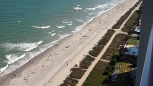 Una playa con una extensa franja de arena, un muelle a lo lejos y un edificio con piscina a la derecha.