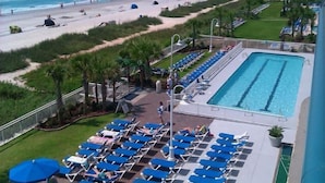 Zona de piscina con sillas reclinables azules y vista a la playa y al océano.