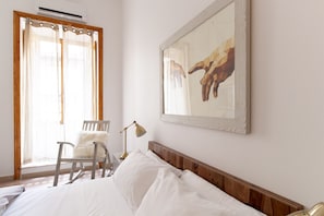 Relax in a serene space with a comfortable bed, a stylish chair, and a floor lamp, set against a backdrop of a large abstract painting.
