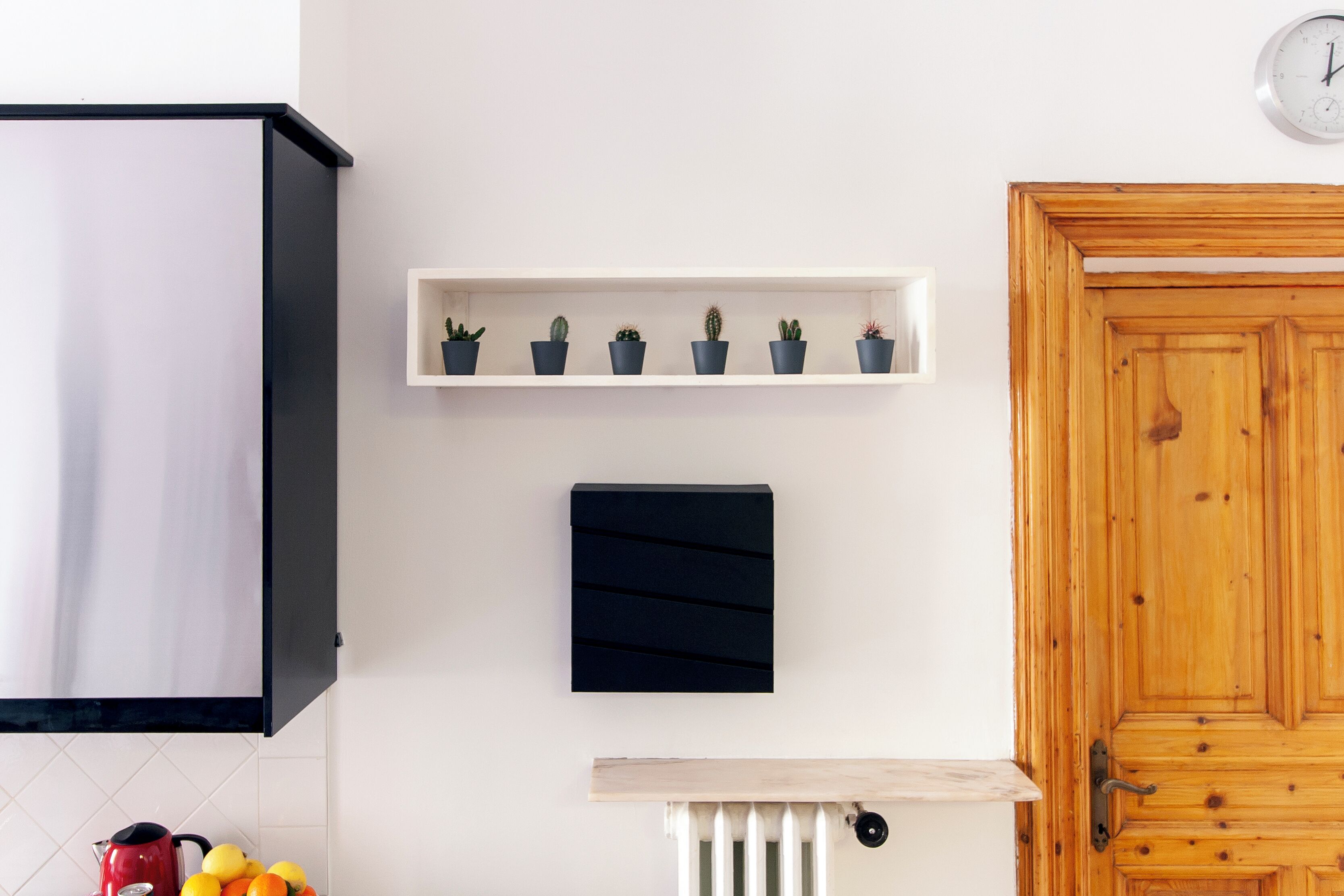 A kitchen with a white cabinet, a black panel, a wooden door, a shelf with potted plants, and a radiator.