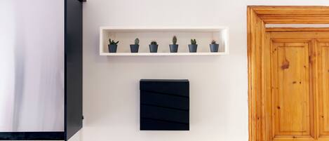 A kitchen with a white cabinet, a black panel, a wooden door, a shelf with potted plants, and a radiator.