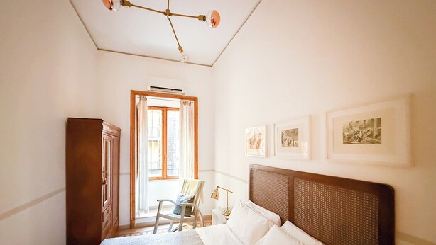 A bedroom with a bed, a chair, a wardrobe, and a ceiling light fixture. - Live Like a Local in a Artful Apartment near the Colosseum (rome)