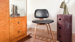 A room with a wooden dresser, a black chair, and a tall purple cabinet with a lamp on top. - Live Like a Local in a Artful Apartment near the Colosseum (rome)