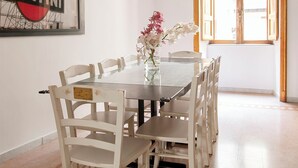 A dining area with a round table, white chairs, a vase with flowers, a hanging light fixture, and a window with wooden shutters. - Live Like a Local in a Artful Apartment near the Colosseum (rome)