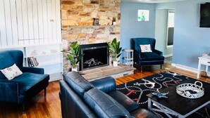 Una sala de estar moderna con chimenea de piedra, sillones azules, sofá de cuero negro y alfombra estampada.