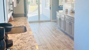 Una cocina amplia con encimera de mármol, suelo de madera y puertas de vidrio correderas que dan a un balcón.