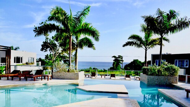 A pool area with lounge chairs and palm trees, overlooking a body of water. - Nautical Homes 3 Ocean Front/View, Free Wifi, A/C, Hot Tub, BBQ Grill. Balcony (Montego bay)