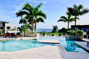 A pool area with lounge chairs and palm trees, overlooking a body of water. - Montego Bay Luxury 3BR Villa Ocean Views & Pool (Montego bay)