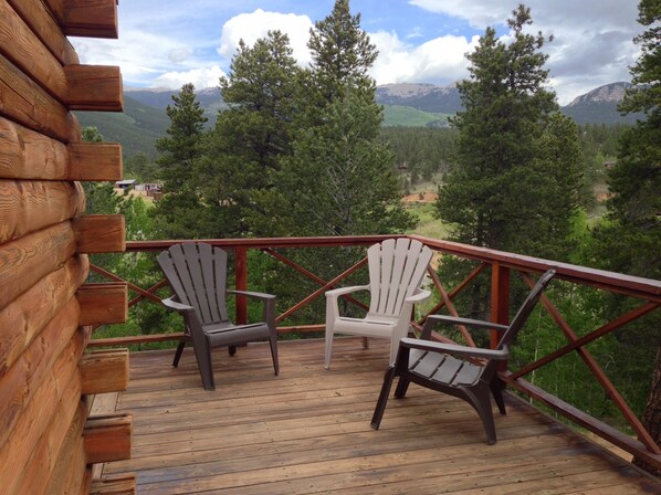A wooden deck with two Adirondack chairs overlooking a mountainous landscape.