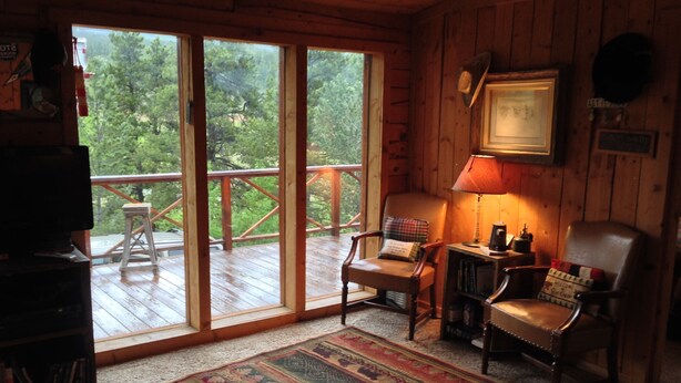 Interior acogedor de una cabaña con un amplio ventanal corredizo que da a una terraza, muebles de madera y una alfombra.