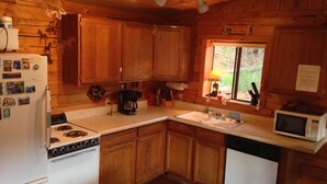Cocina de cabaña de madera con estufa, refrigerador, microondas y pileta.