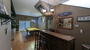 A pool table in a room with a bar area, a ceiling fan, and various wall decorations including a Bud Light sign and a banner. - Great house for making memories! Two living areas, bar, and pool table (Alpine)