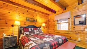 Une chambre chaleureuse aménagée dans un chalet en bois, avec un lit, des lampes de chevet, une petite table et une fenêtre donnant sur un paysage agréable.
