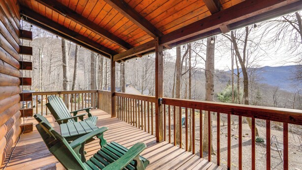 Une terrasse en bois avec une balustrade, deux fauteuils Adirondack verts et une vue sur une forêt et des montagnes.