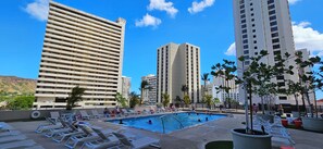 A pool area with lounge chairs and a swimming pool surrounded by tall buildings.