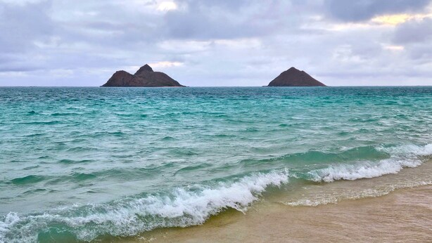 Une plage bordée d’une eau turquoise et, au loin, deux îles rocheuses.