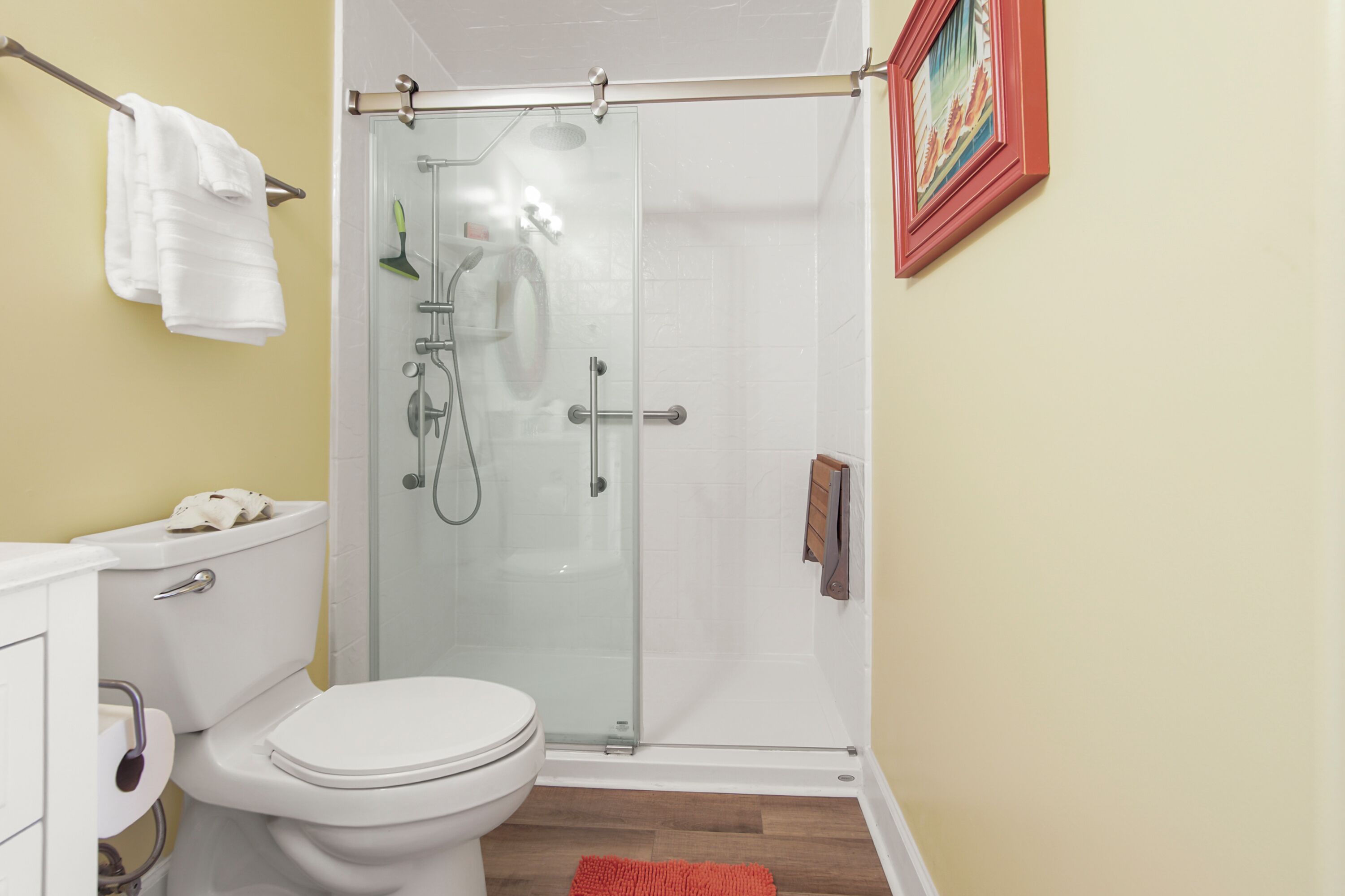 Een badkamer met toilet, douchecabine van glas en een rood vloerkleed.