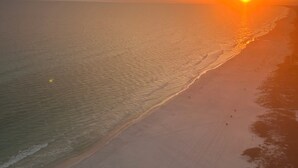 A beach with a sunset, calm sea, and clear sky.