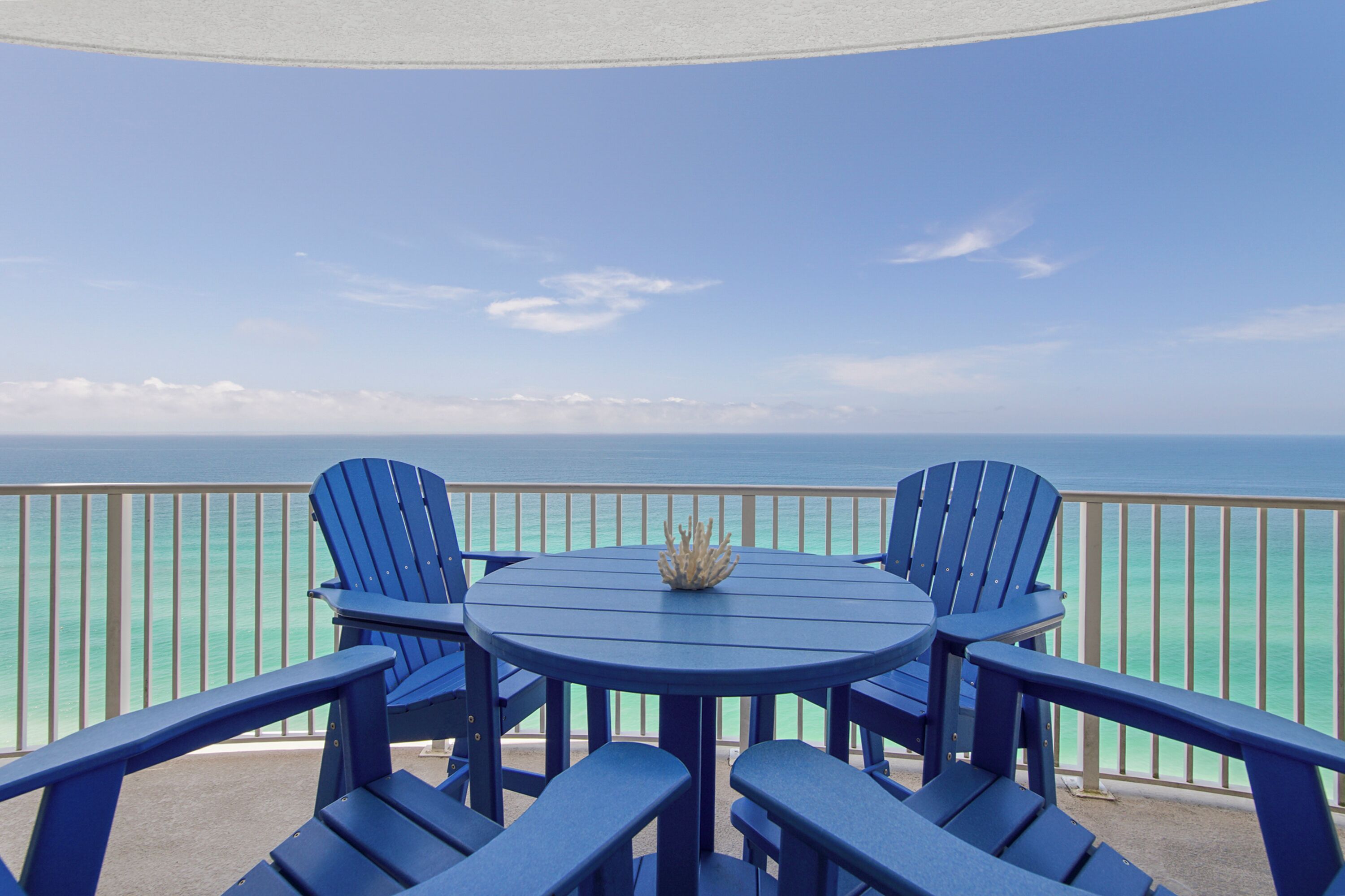 Una mesa redonda con cuatro sillas Adirondack azules, un centro de mesa decorativo y vista al océano.