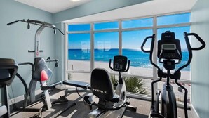 A gym with a view of the beach, equipped with cardio machines and weightlifting equipment.