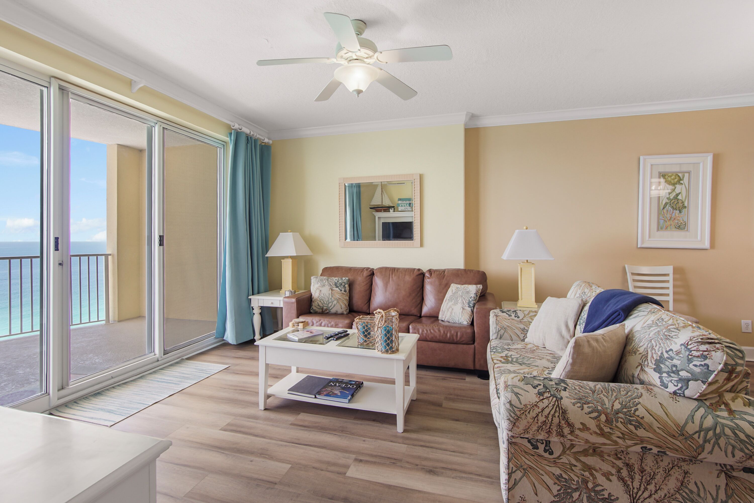 A living room with a sofa, a coffee table, a ceiling fan, and a large window with a view.