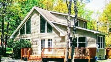 Situated in a wooded area, this cabin features a front porch with a bench and multiple windows offering views of the surrounding forest.