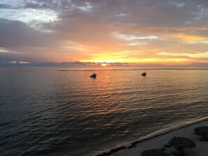 Una playa con dos barcos en aguas tranquilas durante el atardecer.