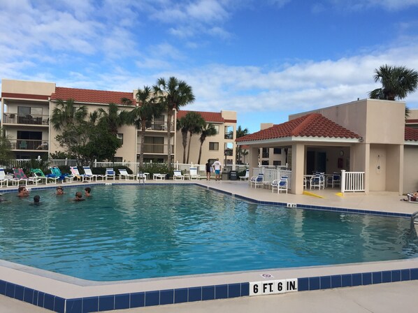 Una piscina con una profundidad de 6 pies 6 pulgadas, rodeada de sillas de descanso y palmeras, con un edificio al fondo.