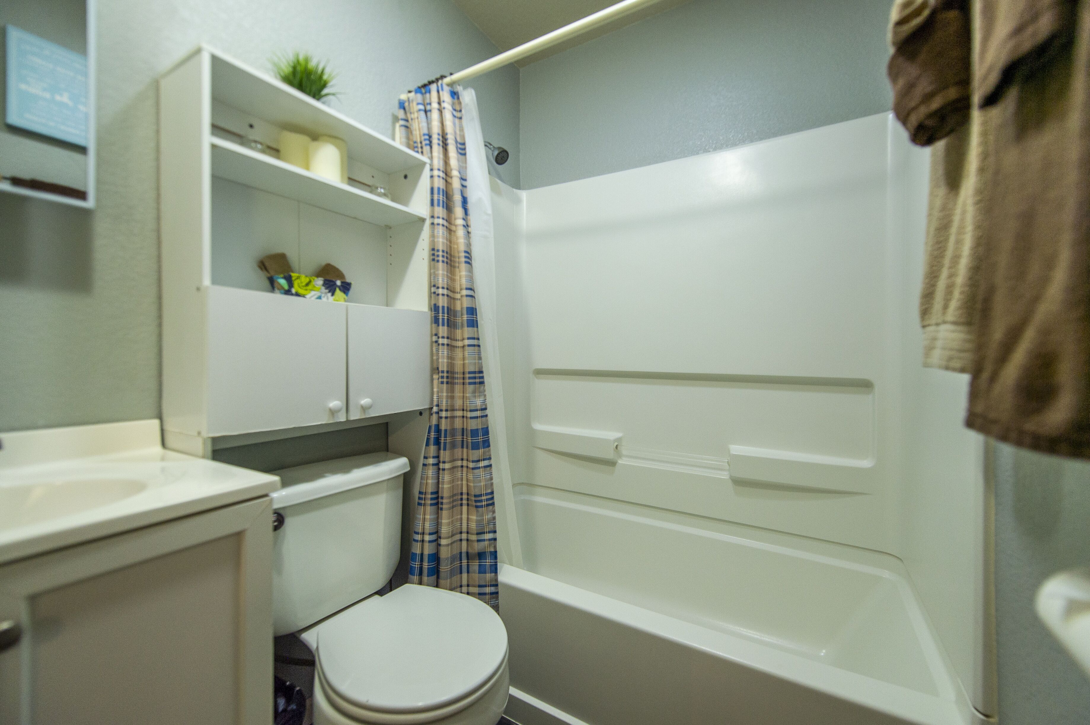 A bathroom with a toilet, a sink, a shower, and a shelf with toiletries.