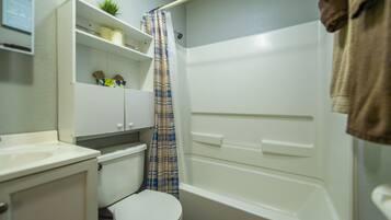 A bathroom with a toilet, a sink, a shower, and a shelf with toiletries.
