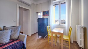 Une pièce comprenant un canapé, deux fauteuils jaunes, une table, un buffet bleu et une fenêtre donnant sur des immeubles.