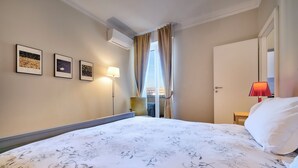 Une chambre d’hôtel avec un grand lit, un bureau avec une chaise, une fenêtre avec des rideaux et trois tableaux encadrés accrochés au mur.