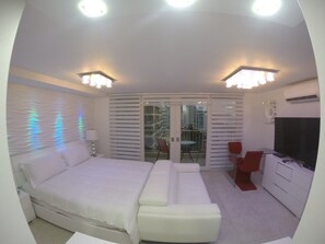 Habitación de hotel moderna con cama, sofá, televisión y balcón con mesa y sillas.