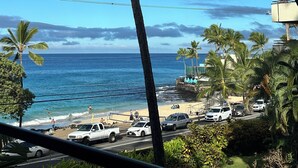 Blick auf einen Strand mit Palmen, einem wolkenlosen Himmel und einer Straße mit geparkten Autos.