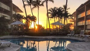 Ein Swimmingpool mit Palmen und einem Sonnenuntergang im Hintergrund.