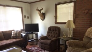 Un salon comprenant un canapé, un fauteuil, un téléviseur et une tête de cerf fixée au mur.